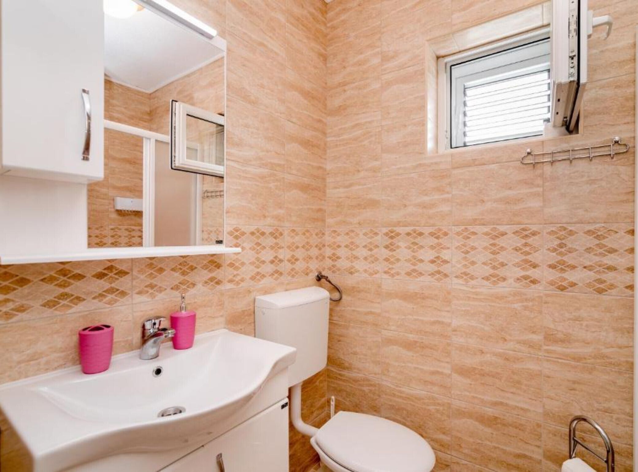 Ein Badezimmer mit einem weißen Waschbecken, einer Toilette und einem Fenster mit Jalousien.