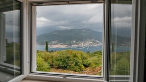 Ein Fenster mit Blick auf eine Küstenstadt, Berge und eine Wasserfläche.