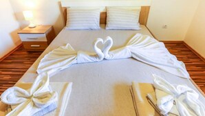 A hotel room with a neatly made bed, two pillows, a bedside table with a lamp, and a wooden floor. - Beachfront Escape – Steps from the Crystal-Clear Sea - One Bedroom Apartment (Bogisici)