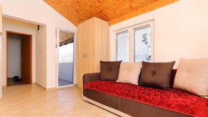 Un soggiorno moderno con soffitto in legno, un divano marrone con cuscini decorati e una porta vetrata scorrevole che dà su un balcone.