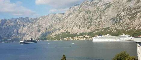A coastal town with traditional buildings, a large cruise ship docked, and a mountainous backdrop.