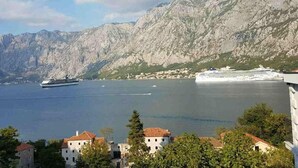 Eine Küstenstadt mit traditioneller Architektur, einem großen Kreuzfahrtschiff im Hafen und einem Bergpanorama im Hintergrund.
