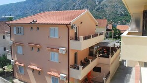 A multi-story building with balconies, air conditioning units, and a mountainous backdrop. - Chic & Sleek Apartments in Kotor - Studio Apartment with Balcony (Kotor)