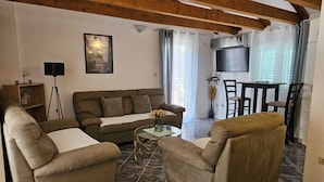 A living room with a sofa, armchairs, a coffee table, a TV, and a dining area with chairs and a table.