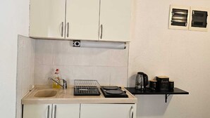A compact kitchen with white cabinets, a sink, a stove, and a small shelf with kitchen items.
