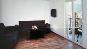 Un salon avec un canapé noir, une table basse agrémentée d’un arrangement floral et un téléviseur fixé au mur.