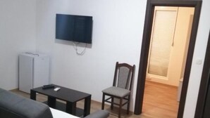 Un salon avec un téléviseur à écran plat fixé au mur, une petite table, une chaise et une porte-fenêtre donnant sur une autre pièce.