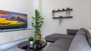 A modern living room with a flat-screen TV, a large potted plant, a grey sofa, and a coffee table. - Two Bedroom Apartment with Balcony (Zadar)