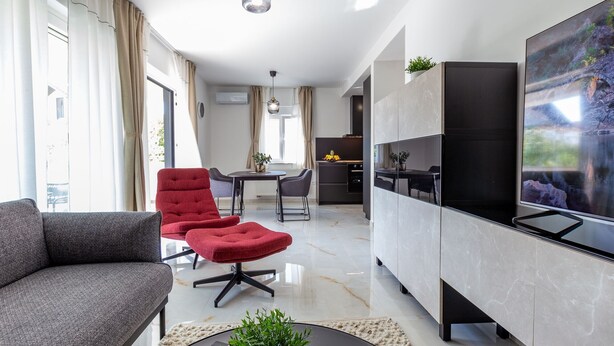 A modern living room with a sofa, red armchair, and a dining area with a table and chairs. - Two Bedroom Apartment with Balcony (Zadar)