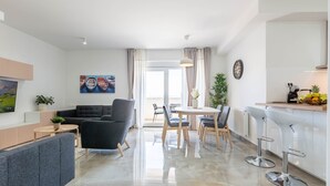 A modern living room with a sofa, a dining table with chairs, and a kitchen area with bar stools. - Three Bedroom Apartment with Balcony (Zadar)