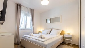 A neatly arranged bedroom with a bed, bedside tables, a mirror, and a window with curtains. - Three Bedroom Apartment with Balcony (Zadar)