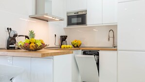 Uma cozinha moderna com armários brancos, bancada de madeira, uma fruteira, cafeteira e lava-louças.