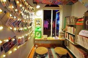 A cozy reading nook with a wall of books, a small table with a lamp, and a window with a view. - Yangshuo Lazy People's Hall Inn (West Street Lijiang Branch) (Yangshuo)