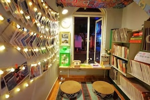 A cozy reading nook with bookshelves, a window, and a wall adorned with framed photos and string lights.