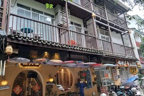 A traditional building with a balcony, multiple windows, and a storefront with umbrellas. - Yangshuo Lazy People's Hall Inn (West Street Lijiang Branch) (Yangshuo)