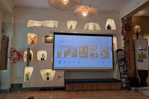 A hotel lobby with a large screen displaying a digital interface, a seating area, and various wall decorations.
