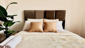 Una cama bien hecha con un edredón texturizado, dos almohadas y una toalla enrollada.