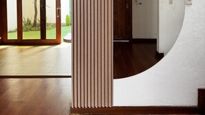 Un pasillo con un pilar de madera, una pared blanca con un recorte circular y una puerta que dice "GARAGE".