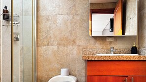 Un baño con cabina de ducha de vidrio, inodoro, lavamanos con encimera de granito y mueble de madera.