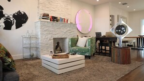 Un salon moderne avec une cheminée, un fauteuil vert, une table basse et une bibliothèque.