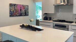 Une cuisine moderne dotée d’un îlot central, d’appareils électroménagers en acier inoxydable et d’un grand tableau abstrait accroché au mur.