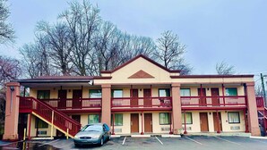 A two-story motel with a red exterior, a central entrance, and a parking lot with a car.