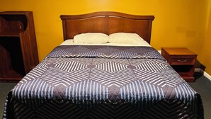 A neatly made bed with a patterned bedspread, a wooden headboard, and a bedside table with a drawer.