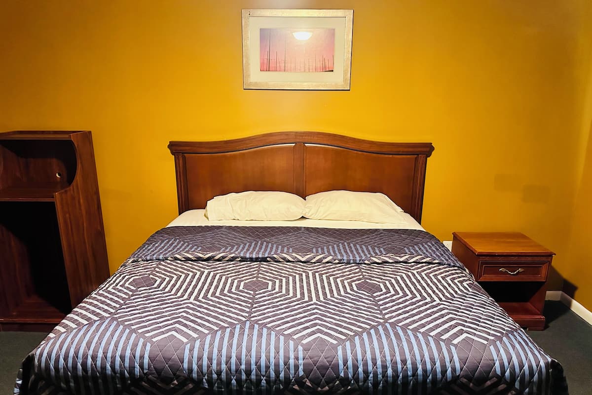 A neatly made bed with a patterned bedspread, a wooden headboard, and a bedside table with a drawer.