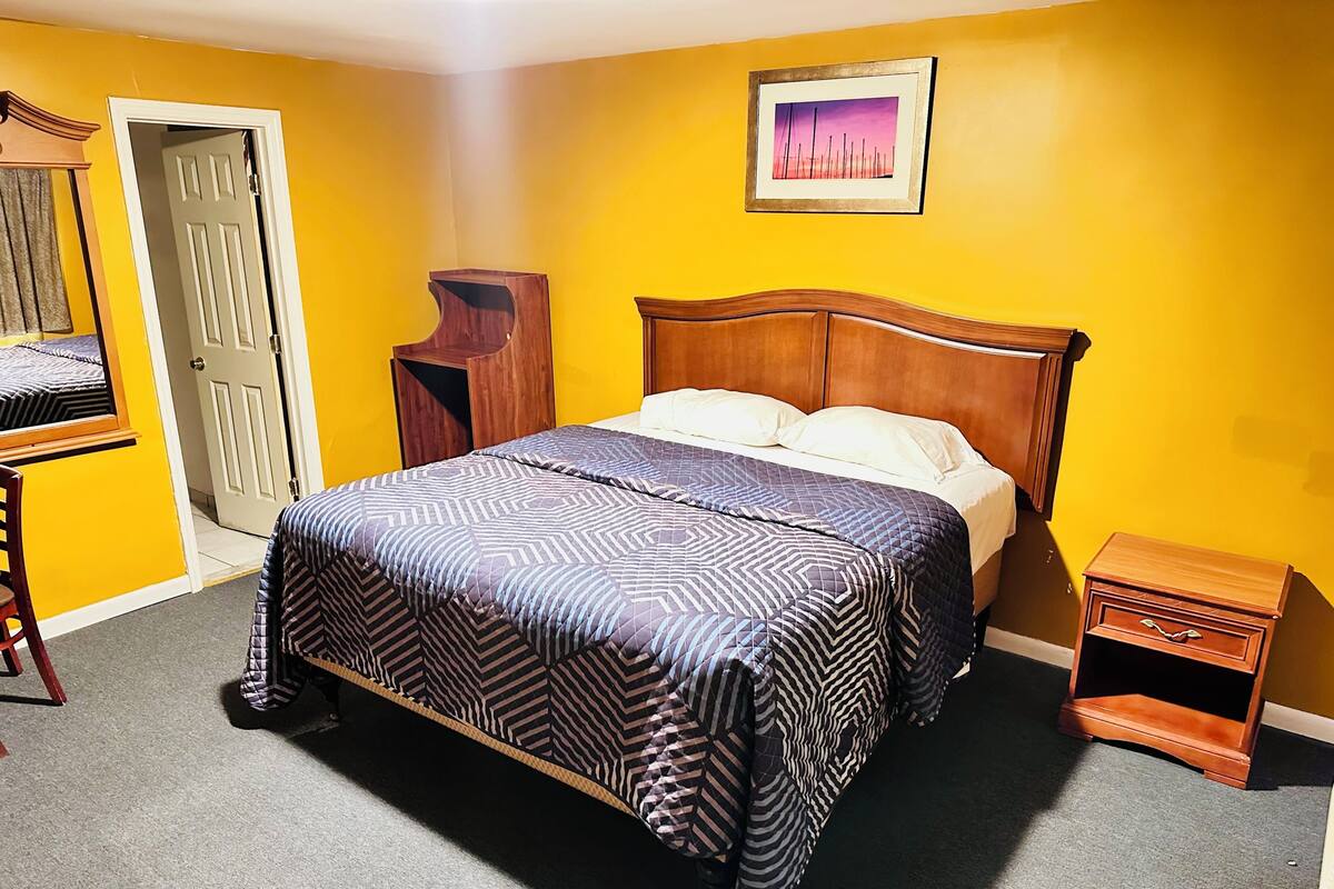 A bedroom with a bed, a nightstand, a dresser, a mirror, and a door.