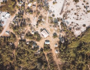 An aerial view of a remote, sparsely populated area with scattered structures, including small buildings and tents, surrounded by dense vegetation and a dirt road. - Crania Reclaim Camp (San José del Cabo)