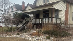 Ein zweistöckiges Haus mit Veranda, einer Treppe zum Eingang und einem Schotterweg.