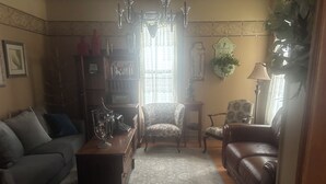 Ein Wohnzimmer mit einer Couch, einem Sessel und einem Couchtisch. Es gibt eine Chandelieber, eine Lampe und einen Topfpflanzen.