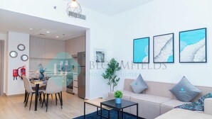 A modern living room with a sofa, coffee table, and dining area. There are three framed pictures on the wall, a small plant on the coffee table, and a blue rug on the floor. - Bloomfields Fantastic 1BR in Waters edge (Abu Dhabi)