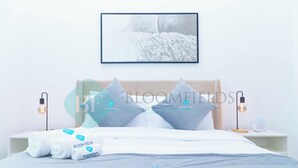 A neatly made bed with white linens, two pillows, and a set of towels with a logo. There is a framed picture on the wall above the bed, and two bedside lamps on either side. - Bloomfields Fantastic 1BR in Waters edge (Abu Dhabi)