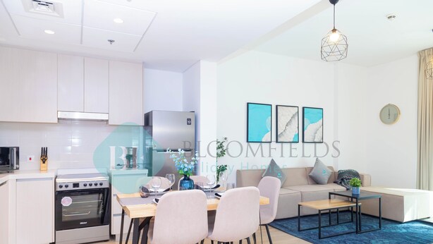 A modern kitchen with built-in appliances, a dining area with a table and chairs, and a living area with a sofa and a coffee table. - Bloomfields Fantastic 1BR in Waters edge (Abu Dhabi)