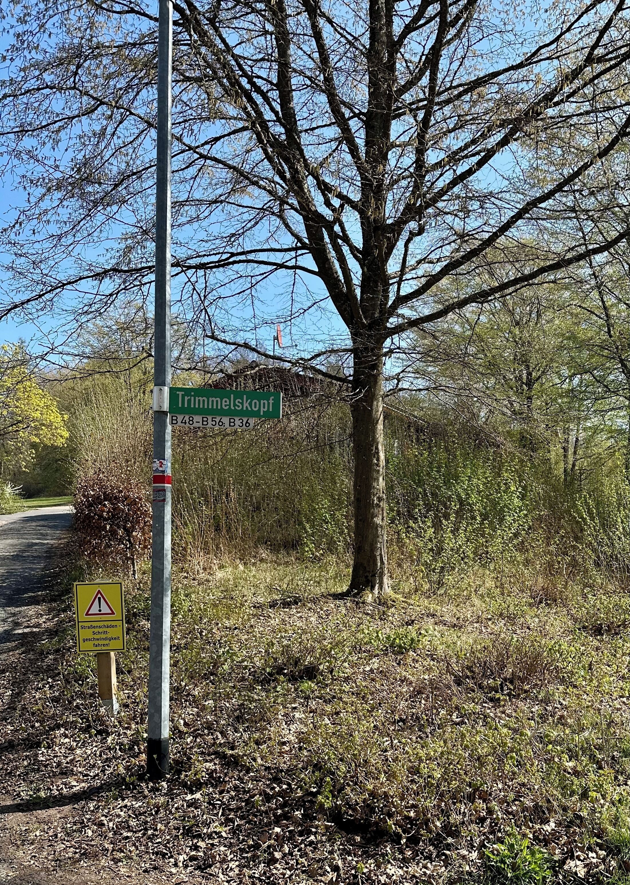 A street sign for 'Trimmelskopf' with a warning sign below it.