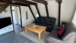 A modern loft-style living room with a black leather sofa, a wooden coffee table, and a grey rug. - Pure nature - forest vacation in a tiny house (Ronshausen)