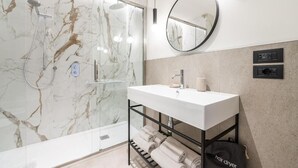 A modern bathroom with a marble shower, a white sink, a mirror, and a hair dryer on the floor.