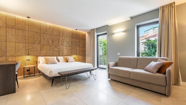 A modern hotel room with a large bed, a sofa, a desk, and a patterned wall.