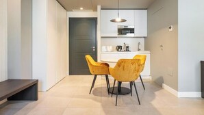 A modern kitchen with white cabinets, a microwave, and a coffee maker. There are two yellow chairs and a bench in the dining area.