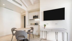 A modern kitchen with white cabinets, a built-in oven, and a flat-screen TV mounted on the wall. - JUNIOR SUITE DOUBLE BED (Cagliari)