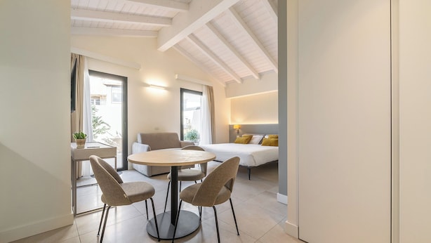 A modern interior with a dining area, a sofa, and a bed. - JUNIOR SUITE DOUBLE BED (Cagliari)