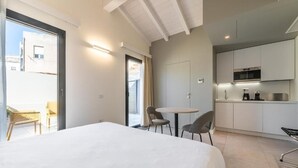 A modern hotel room with a large bed, a small dining table, and a kitchenette. - Deluxe Double Room (Cagliari)