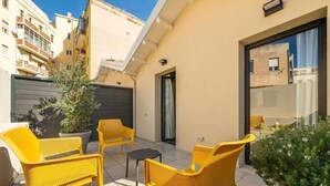 A small outdoor patio area with yellow wicker furniture, a potted plant, and a view of neighboring buildings. - Deluxe Double Room (Cagliari)