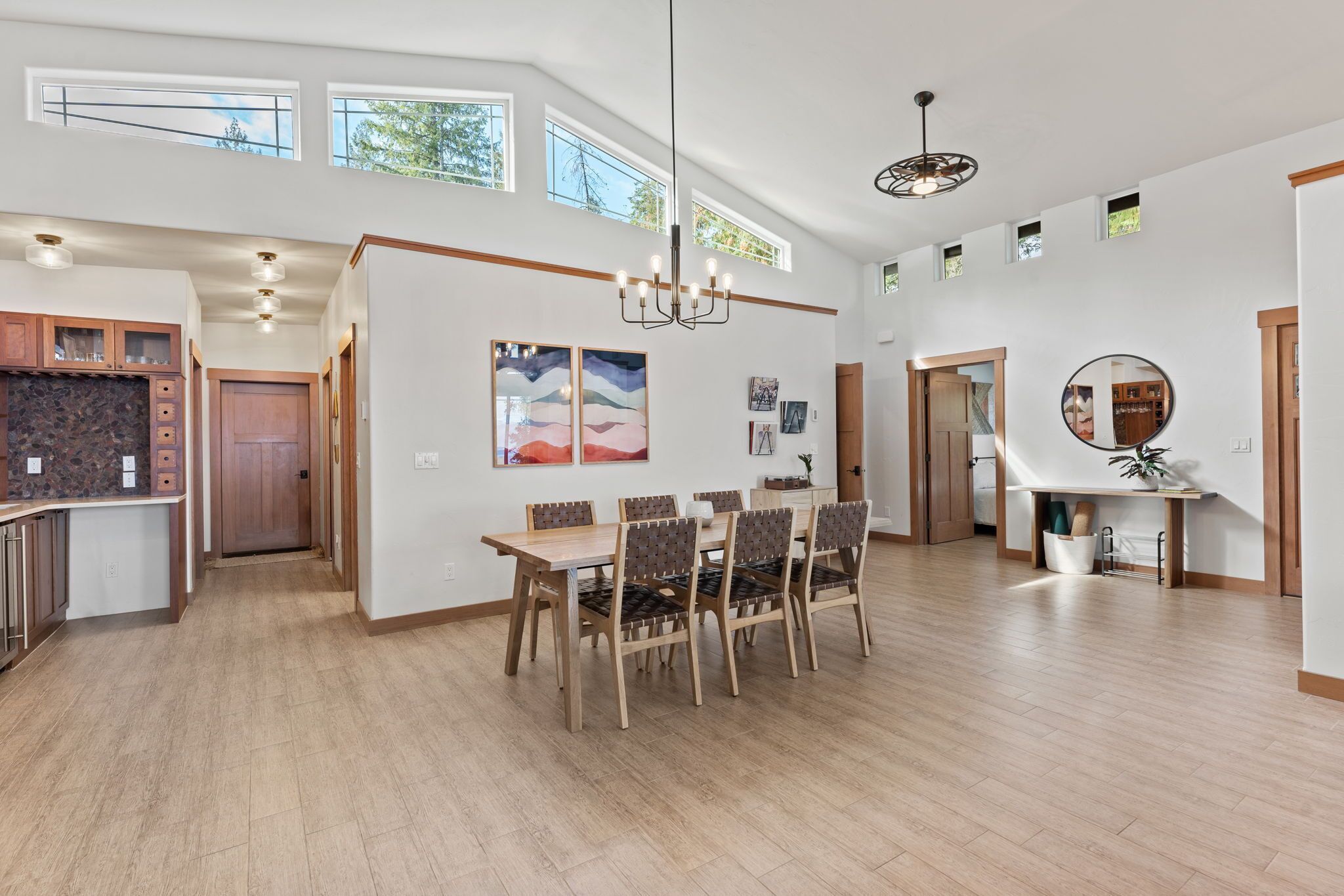 A spacious, well-lit interior with a high ceiling, a dining area with wooden chairs and a table, and a kitchen with wooden cabinets.