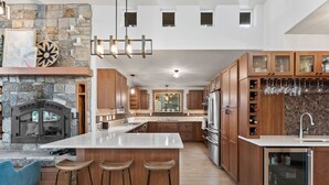 A modern kitchen with a central island, wooden cabinets, a stone fireplace, and a wine rack. - Beautiful Waterfront Cabin with a Hot Tub & Sauna (Nordman)