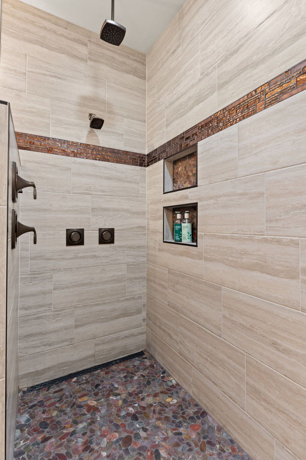 Zona doccia con soffione a pioggia, doccetta manuale e ripiano con articoli da toilette.