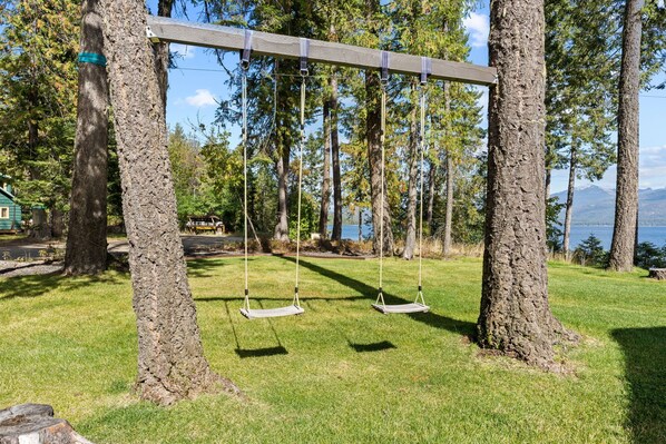 Un ensemble de balançoires en bois installé dans un espace verdoyant, avec des arbres et un lac en arrière-plan.