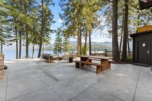 Un patio con tavolo e panche in legno, circondato da alberi alti e vista su un lago.