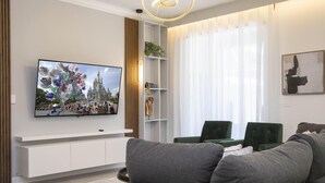 A modern living room with a flat-screen TV mounted on the wall, a grey sofa, and a green armchair.